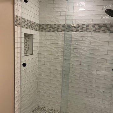 3x12 textured subway tile, with a darker mosaic band and pebble shower floor.