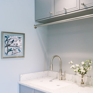 ポートランド(メイン)のトランジショナルスタイルのおしゃれなランドリールーム (再生ガラスカウンター、磁器タイルの床、アンダーカウンターシンク、青い壁、左右配置の洗濯機・乾燥機、グレーのキャビネット) の写真