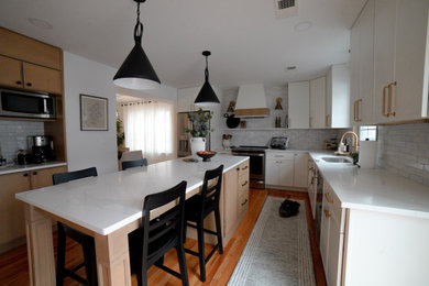Inspiration for a mid-sized transitional l-shaped medium tone wood floor eat-in kitchen remodel in New York with a drop-in sink, shaker cabinets, white cabinets, granite countertops, beige backsplash, subway tile backsplash, stainless steel appliances, an island and white countertops