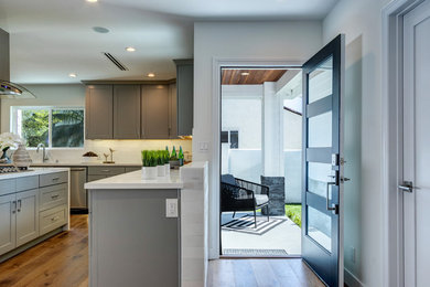 Example of a large minimalist l-shaped medium tone wood floor open concept kitchen design in Los Angeles with a double-bowl sink, shaker cabinets, gray cabinets, quartzite countertops, white backsplash, subway tile backsplash, stainless steel appliances, an island and white countertops