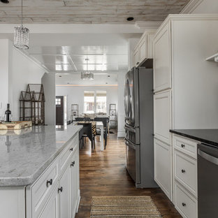 Новый формат декора квартиры: маленькая угловая кухня в стиле современная классика с обеденным столом, врезной раковиной, фасадами с утопленной филенкой, белыми фасадами, столешницей из гранита, черным фартуком, фартуком из сланца, техникой из нержавеющей стали, паркетным полом среднего тона, островом, коричневым полом и черной столешницей