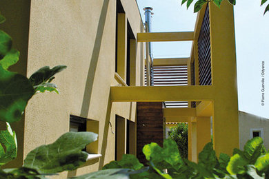 This is an example of an expansive contemporary two-storey yellow house exterior in Marseille with wood siding, a flat roof and a green roof.