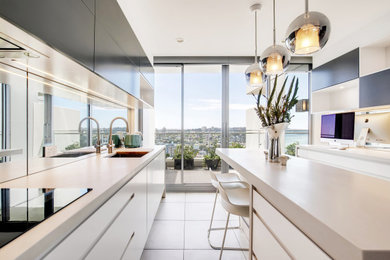 This is an example of a large modern galley eat-in kitchen in Sydney with an undermount sink, flat-panel cabinets, white cabinets, quartz benchtops, metallic splashback, glass sheet splashback, stainless steel appliances, porcelain floors, with island, grey floor and grey benchtop.