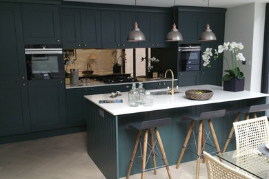 Example of a mid-sized classic single-wall eat-in kitchen design in Berkshire with an undermount sink, shaker cabinets, green cabinets, quartzite countertops, metallic backsplash, glass sheet backsplash, black appliances and an island