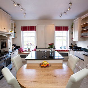 Large traditional kitchen pantry ideas - Inspiration for a large timeless u-shaped kitchen pantry remodel in Kent with a farmhouse sink, beaded inset cabinets, white cabinets, granite countertops, black backsplash, stone slab backsplash, stainless steel appliances and an island