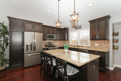 Example of a mid-sized transitional l-shaped medium tone wood floor and brown floor eat-in kitchen design in Chicago with a double-bowl sink, recessed-panel cabinets, dark wood cabinets, granite countertops, brown backsplash, glass tile backsplash, an island and colored appliances