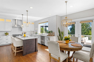 Eat-in kitchen - mid-sized coastal u-shaped brown floor and dark wood floor eat-in kitchen idea in Seattle with an undermount sink, shaker cabinets, white cabinets, white backsplash, subway tile backsplash, stainless steel appliances, an island, white countertops and quartz countertops
