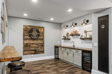 Inspiration for a mid-sized country seated home bar in Columbus with a drop-in sink, shaker cabinets, white cabinets, wood benchtops, white splashback, timber splashback, porcelain floors, brown floor and brown benchtop.