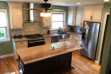Example of a mid-sized classic l-shaped medium tone wood floor and brown floor enclosed kitchen design in Philadelphia with white cabinets, an island, brown countertops, a farmhouse sink, recessed-panel cabinets, granite countertops, beige backsplash, stone tile backsplash and stainless steel appliances