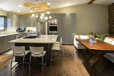 Eat-in kitchen - contemporary l-shaped medium tone wood floor eat-in kitchen idea in Seattle with flat-panel cabinets, gray cabinets, quartz countertops, white backsplash and stainless steel appliances