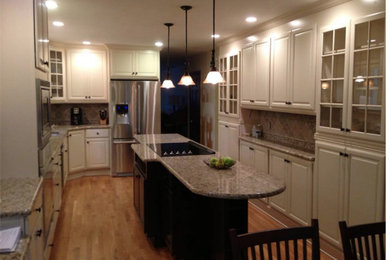 Mid-sized transitional l-shaped medium tone wood floor eat-in kitchen photo in Wilmington with an undermount sink, raised-panel cabinets, white cabinets, granite countertops, beige backsplash, stone tile backsplash, stainless steel appliances and an island