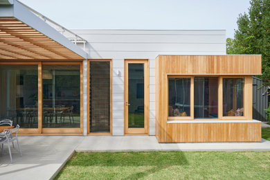 This is an example of a mid-sized contemporary grey house exterior in Adelaide with wood siding, a flat roof, a metal roof, a grey roof and board and batten siding.