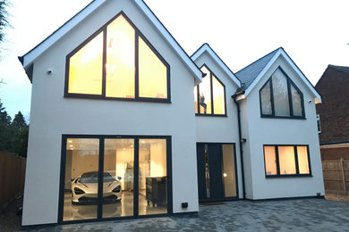 This is an example of an expansive and white modern detached house in Buckinghamshire with three floors, a pitched roof, a tiled roof and a black roof.