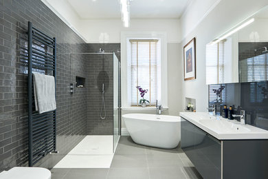 Mid-sized modern kids bathroom in Hertfordshire with glass-front cabinets, grey cabinets, a freestanding tub, an open shower, a wall-mount toilet, gray tile and an open shower.