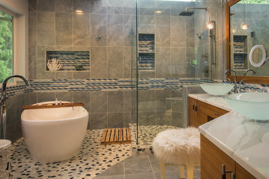 Photo of a large modern master wet room bathroom in Seattle with flat-panel cabinets, medium wood cabinets, a freestanding tub, a one-piece toilet, blue tile, gray tile, multi-coloured tile, white tile, stone tile, white walls, mosaic tile floors, a vessel sink, marble benchtops, multi-coloured floor and a hinged shower door.