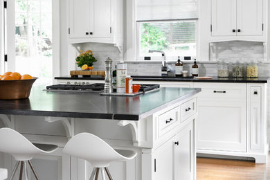 Example of a transitional medium tone wood floor open concept kitchen design in Atlanta with an undermount sink, white cabinets, soapstone countertops, white backsplash, stone tile backsplash, stainless steel appliances, shaker cabinets and an island
