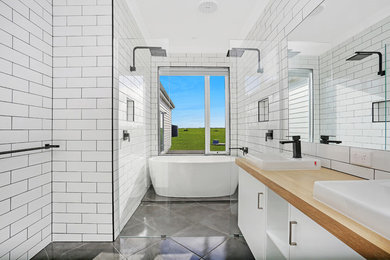 Photo of an industrial master bathroom in Melbourne with white cabinets, a freestanding tub, a double shower, a one-piece toilet, white tile, subway tile, white walls, ceramic floors and laminate benchtops.