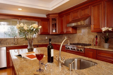 Mid-sized elegant l-shaped medium tone wood floor enclosed kitchen photo in Boston with an undermount sink, raised-panel cabinets, medium tone wood cabinets, granite countertops, white backsplash, stone slab backsplash, stainless steel appliances and an island