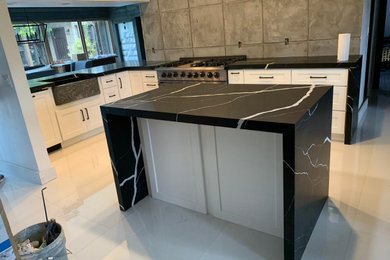 Inspiration for a mid-sized contemporary l-shaped eat-in kitchen in Miami with a farmhouse sink, shaker cabinets, white cabinets, quartz benchtops, grey splashback, cement tile splashback, stainless steel appliances, porcelain floors, with island, white floor and black benchtop.