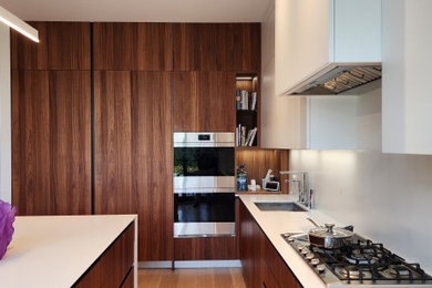 Bild på ett avskilt, stort funkis vit linjärt vitt kök, med en undermonterad diskho, släta luckor, skåp i mörkt trä, bänkskiva i kvarts, vitt stänkskydd, mellanmörkt trägolv och brunt golv