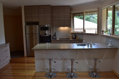 Inspiration for a small contemporary galley eat-in kitchen in Melbourne with an undermount sink, flat-panel cabinets, glass sheet splashback, stainless steel appliances, medium hardwood floors and with island.