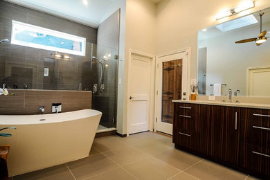 This is an example of a modern master bathroom in Dallas with flat-panel cabinets, medium wood cabinets, a freestanding tub, a double shower, a one-piece toilet, gray tile, porcelain tile, grey walls, porcelain floors, an undermount sink, engineered quartz benchtops, grey floor, a hinged shower door and grey benchtops.