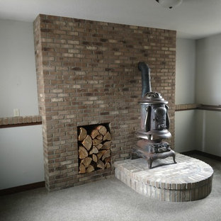 Photo of a medium sized traditional look-out basement in Other with white walls, carpet, a wood burning stove, a brick fireplace surround and grey floors.