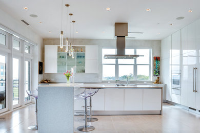 Example of a trendy porcelain tile and beige floor eat-in kitchen design in Miami with an undermount sink, flat-panel cabinets, white cabinets, quartz countertops, white backsplash, stone slab backsplash, white appliances and an island