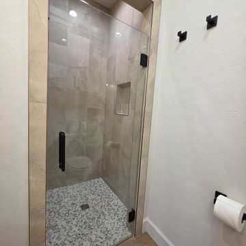 Main Bath Shower surrounded in warm toned porcelain tile and pebble flooring