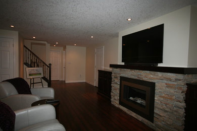 Family room library - mid-sized craftsman dark wood floor family room library idea in Toronto with beige walls, a standard fireplace, a stone fireplace and a wall-mounted tv