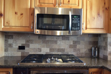 Example of a mid-sized mountain style l-shaped dark wood floor and brown floor eat-in kitchen design in Calgary with an undermount sink, raised-panel cabinets, medium tone wood cabinets, granite countertops, gray backsplash, stone tile backsplash, stainless steel appliances and an island