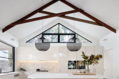 Photo of a mid-sized contemporary l-shaped kitchen in Melbourne with flat-panel cabinets, white cabinets, beige splashback, medium hardwood floors, brown floor, an undermount sink, panelled appliances and with island.