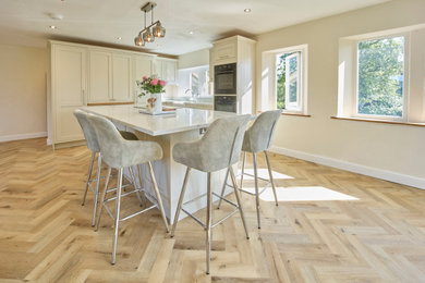 Design ideas for a contemporary open plan kitchen in Other with shaker cabinets, white cabinets, quartz worktops, white splashback, light hardwood flooring, an island, brown floors and white worktops.