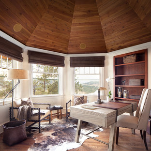 Inredning av ett rustikt mellanstort hemmabibliotek, med vita väggar, mellanmörkt trägolv och ett fristående skrivbord