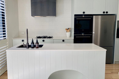 Design ideas for a medium sized contemporary open plan kitchen in Melbourne with a submerged sink, shaker cabinets, engineered stone countertops, matchstick tiled splashback, black appliances, light hardwood flooring and an island.