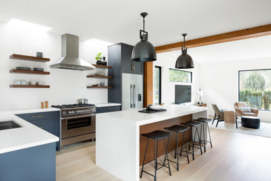 Inspiration for a mid-sized country l-shaped light wood floor and beige floor eat-in kitchen remodel in Vancouver with a farmhouse sink, recessed-panel cabinets, blue cabinets, white backsplash, stone tile backsplash, stainless steel appliances, an island and white countertops