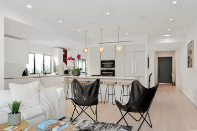 Example of a mid-sized trendy l-shaped light wood floor and beige floor open concept kitchen design in Los Angeles with an undermount sink, flat-panel cabinets, beige cabinets, quartz countertops, white backsplash, stone slab backsplash, stainless steel appliances, an island and white countertops