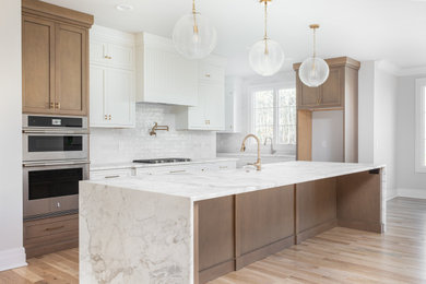 Example of a transitional light wood floor eat-in kitchen design in Other with a farmhouse sink, medium tone wood cabinets, marble countertops, white backsplash, subway tile backsplash, stainless steel appliances, an island and white countertops