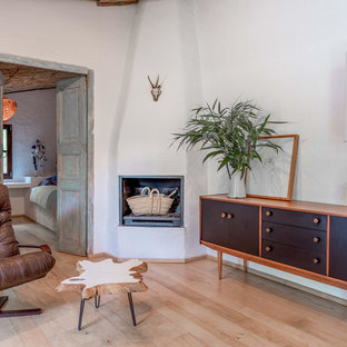 Photo of a mediterranean living room in Barcelona with white walls, light hardwood flooring, a corner fireplace and a plastered fireplace surround.