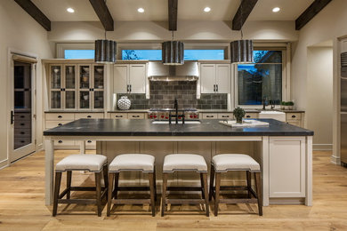 Mid-sized arts and crafts l-shaped light wood floor kitchen photo in Omaha with a farmhouse sink, recessed-panel cabinets, beige cabinets, granite countertops, brown backsplash, glass tile backsplash, stainless steel appliances and an island