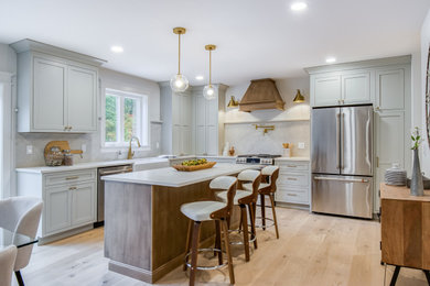 Kitchen - mid-sized l-shaped light wood floor and brown floor kitchen idea in Providence with a farmhouse sink, recessed-panel cabinets, gray cabinets, gray backsplash, stainless steel appliances, an island and white countertops