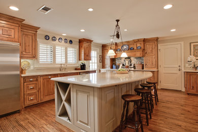 Photo of a large traditional l-shaped open plan kitchen in Dallas with a double-bowl sink, raised-panel cabinets, medium wood cabinets, solid surface benchtops, stainless steel appliances, medium hardwood floors and with island.