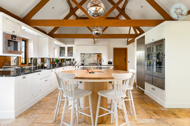 Large modern u-shaped kitchen/diner in Surrey with a built-in sink, white cabinets, quartz worktops, ceramic flooring, an island, brown floors, black worktops, exposed beams and feature lighting.