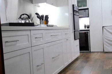 Enclosed kitchen - mid-sized transitional l-shaped porcelain tile and brown floor enclosed kitchen idea in Other with an undermount sink, shaker cabinets, white cabinets, quartz countertops, white backsplash, stainless steel appliances and white countertops