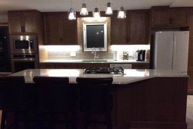 Example of a mid-sized transitional galley eat-in kitchen design in Edmonton with recessed-panel cabinets, medium tone wood cabinets, white backsplash, an island and quartz countertops