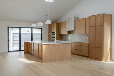 Inspiration for a large mediterranean single-wall light wood floor and vaulted ceiling eat-in kitchen remodel in San Francisco with an undermount sink, flat-panel cabinets, medium tone wood cabinets, quartzite countertops, beige backsplash, stone slab backsplash, stainless steel appliances, an island and beige countertops