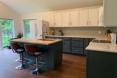Example of a mid-sized transitional l-shaped dark wood floor and brown floor kitchen design in Omaha with an undermount sink, gray backsplash, white appliances, raised-panel cabinets, white cabinets, quartz countertops, ceramic backsplash, an island and white countertops