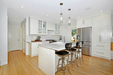 Inspiration for a mid-sized transitional u-shaped light wood floor open concept kitchen remodel in Calgary with a farmhouse sink, raised-panel cabinets, white cabinets, marble countertops, stainless steel appliances and an island