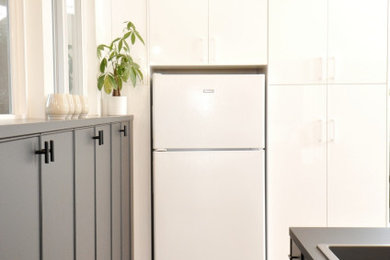 Open concept kitchen - small modern galley vinyl floor and beige floor open concept kitchen idea in San Diego with a drop-in sink, flat-panel cabinets, white cabinets, laminate countertops, white backsplash, white appliances, a peninsula and black countertops