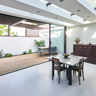 Cette image montre une grande salle à manger ouverte sur le salon traditionnelle avec un mur blanc, béton au sol et aucune cheminée.